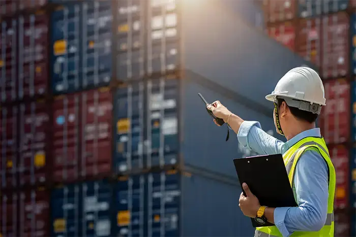 Ceci est une scène d’ambiance dans le port où un ouvrier donne des instructions sur le positionnement des conteneurs.