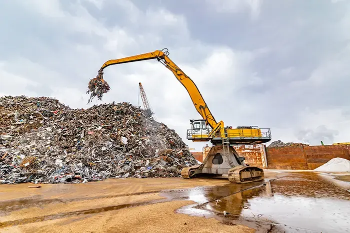 Dit is een sfeerfoto van een hydraulische overslagkraan die actief aan het werk is in de recyclagesector